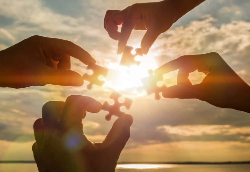 A group of hands holding a puzzle piece in front of the sun, symbolizing the collaboration between the Great Outdoors Fund and Recreation Access in a Public-Private Partnership.