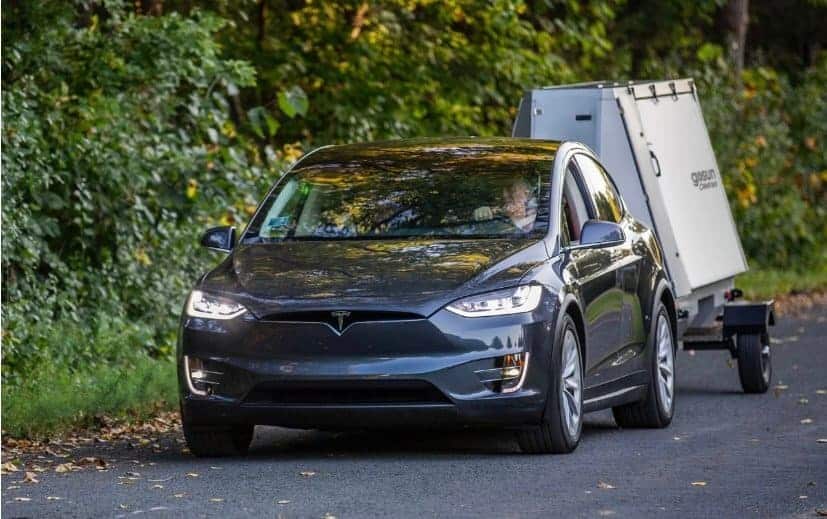 A Tesla Model X is towing an Off-Grid Solar Trailer on the road.