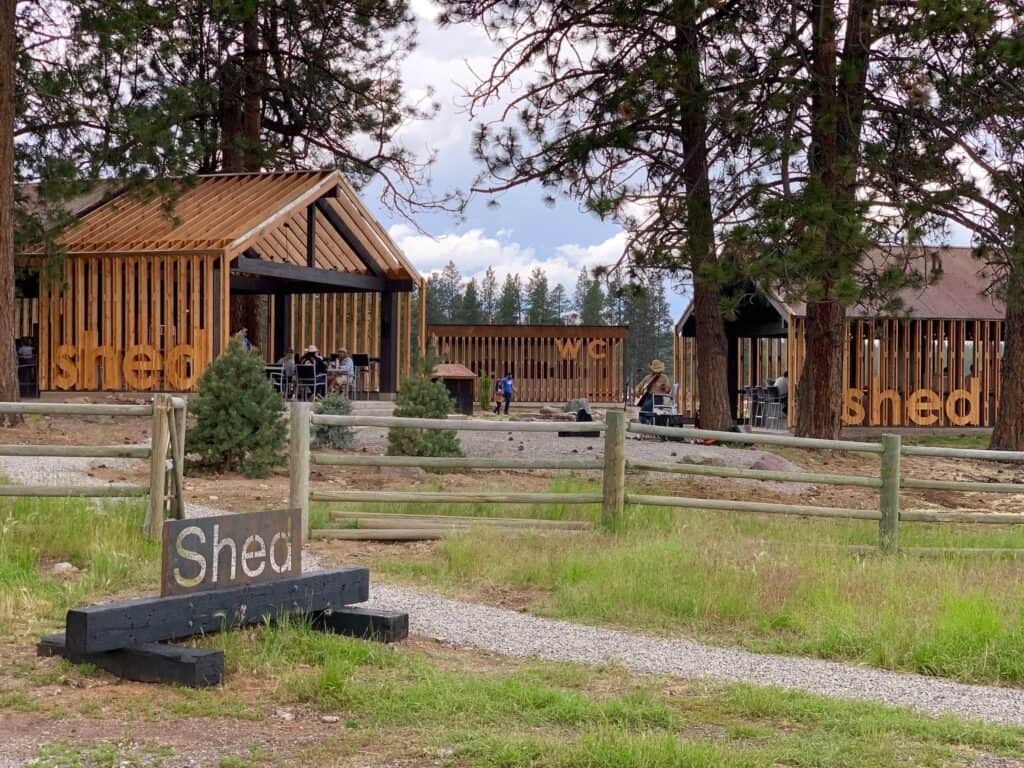 In the midst of a serene wooded area, a simple wooden sign boldly displays the word "Shed." The sign stands as a subtle reminder of the Outdoor Dining Concept at Paws Up.