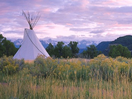 A teepee sits in a field with mountains in the background at Colorado Parks.