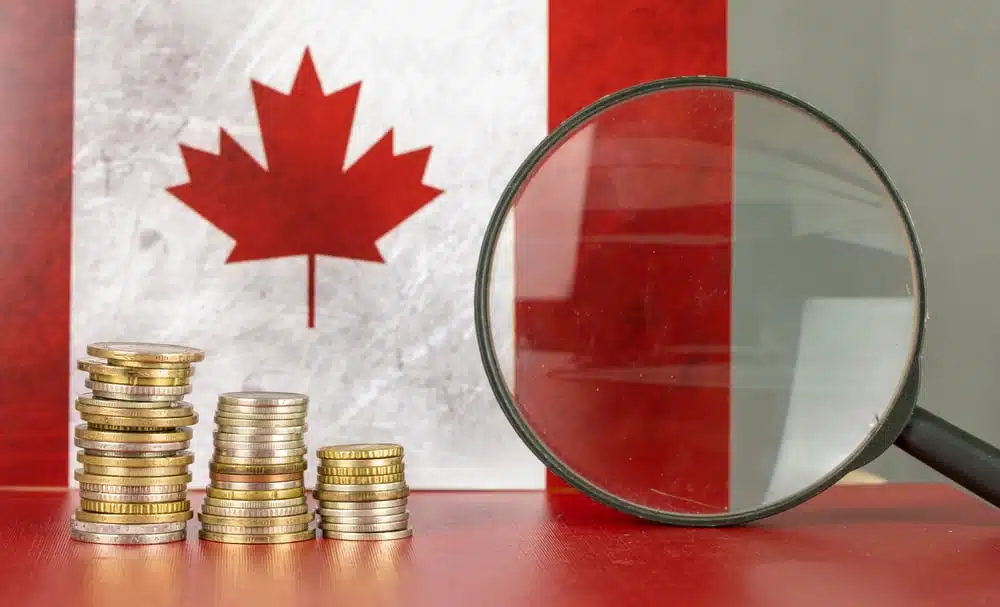 The Canadian flag and stacks of coins with a magnifying glass showcase the impact of inflation rate in Canada.