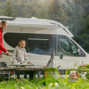 A partner and a group of people sitting around a campfire in front of an RV, enjoying their cross-country traveling journey.