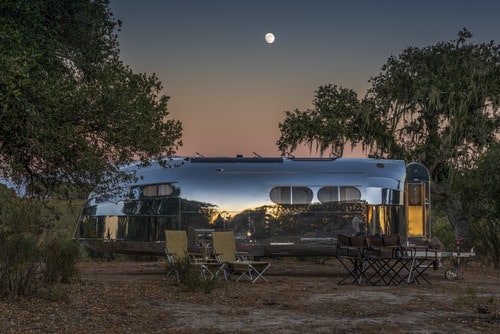 An Ultra-Luxury silver airstream sits in a field at dusk.