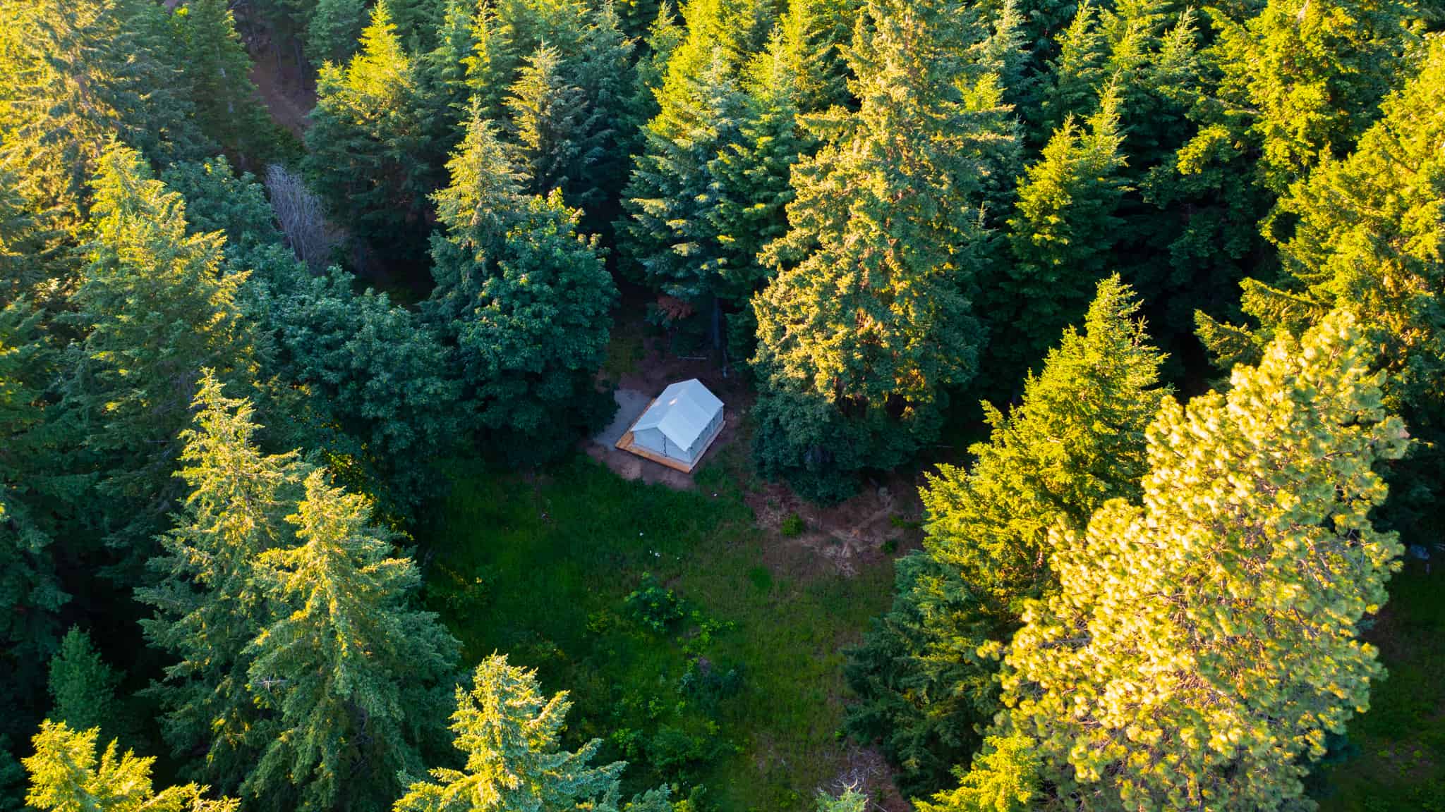 An Uncomplicated Glamping experience awaits at the BaseGlamp ReVivify cabin, nestled in a serene forest. Enjoy the breathtaking aerial view of this cozy retreat surrounded by nature's