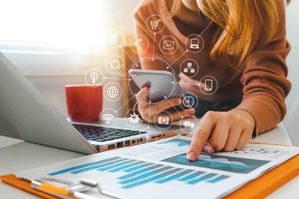 A woman using a smartphone and laptop at her desk while seamlessly integrating with Rollick.