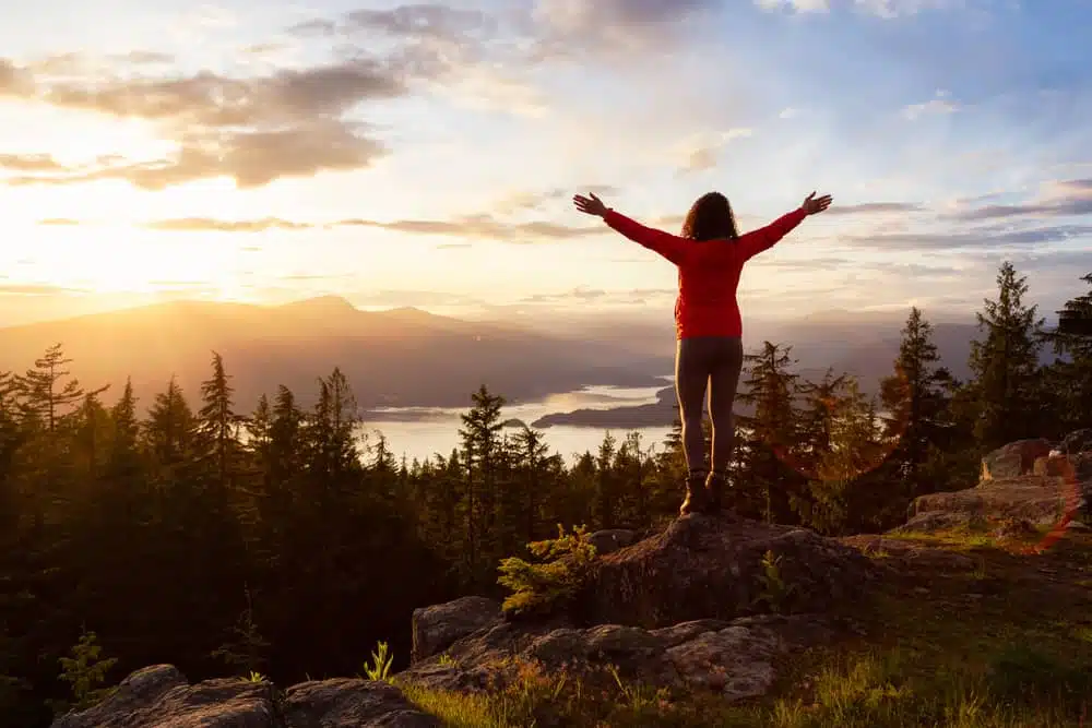 A woman standing on top of Bowen Island's new regional park with her arms outstretched.