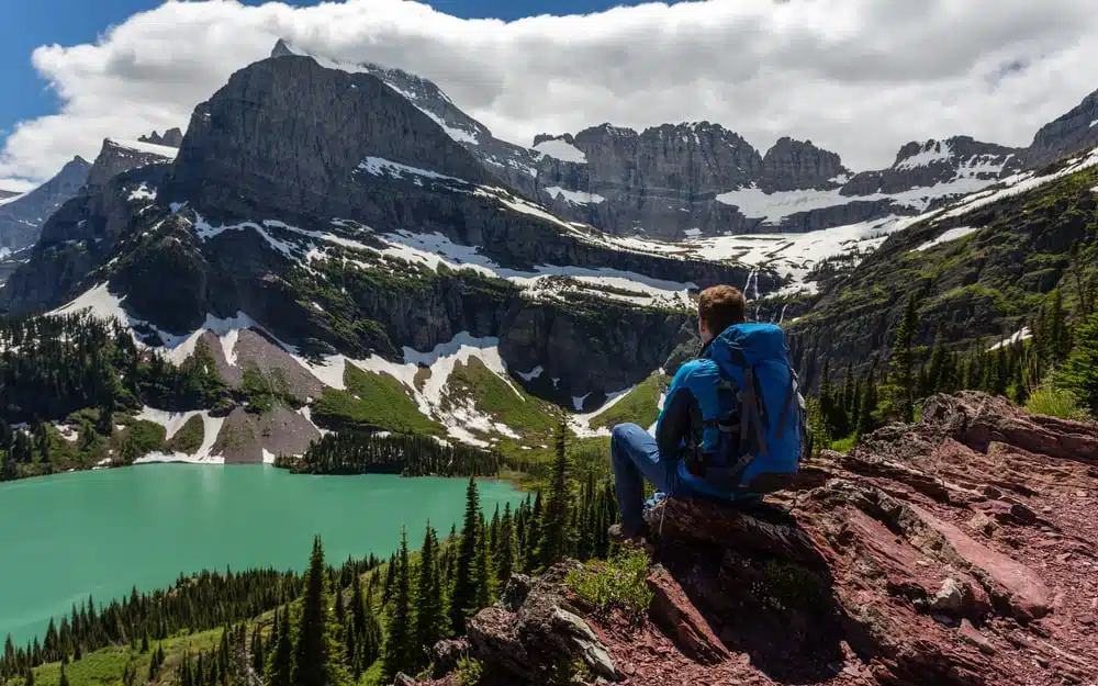 A man enjoys the scenic view while sitting on a rock overlooking a lake in Glacier National Park.