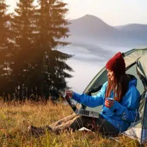 Today's camper is sitting in front of a tent with a laptop, researching tech upgrades.