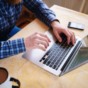 A man typing on a laptop with a cup of coffee, engaged in tech upgrades.