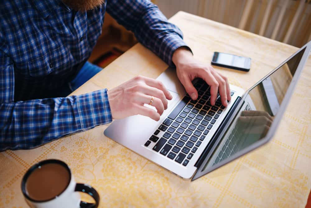 A man typing on a laptop with a cup of coffee, engaged in tech upgrades.