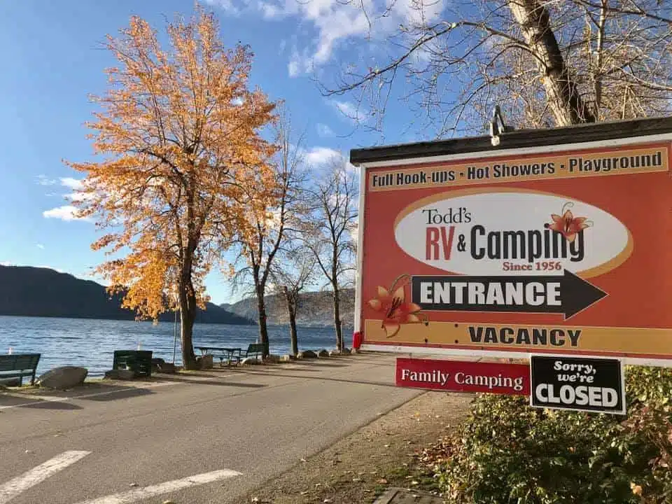 A sign for Todd's RV & Camping bids goodbye in front of a lake.