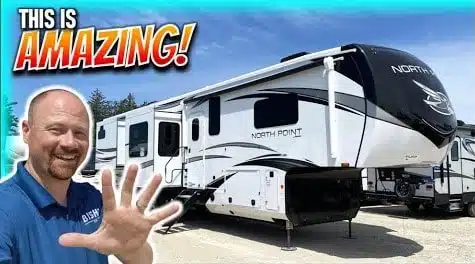 A man is standing in front of a luxurious Fifth-Wheel RV, amazed by its 5-slide design.