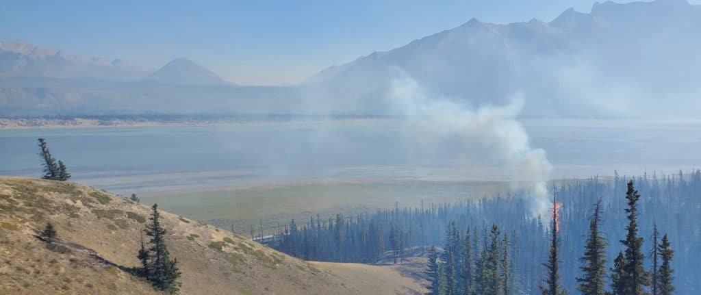 A wildfire is burning in the mountains near a lake.
