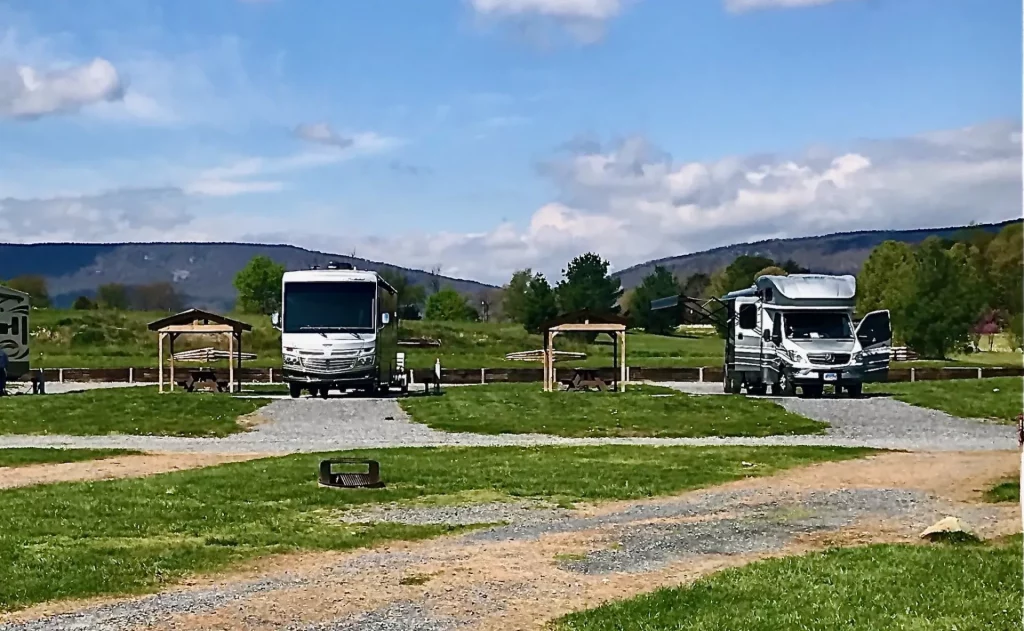 Three RVs parked in the Luray RV Resort, a picturesque campground with majestic mountains in the background, creating a Grand Reveal of nature's beauty.