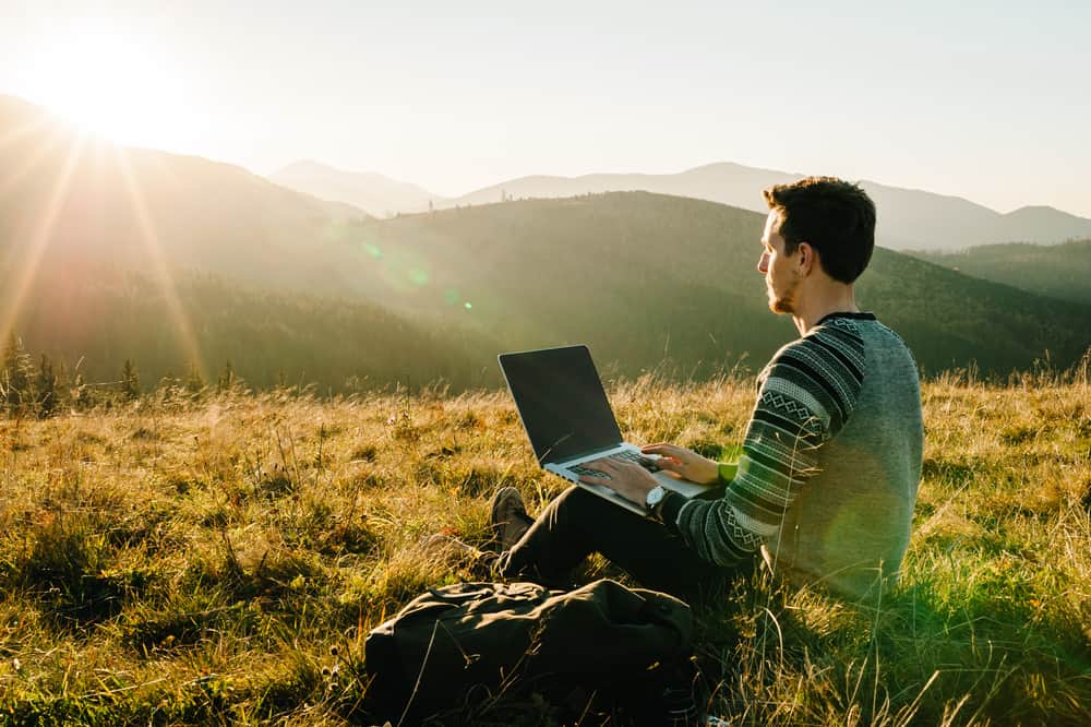 A man sitting on a campground hill with a laptop in his hands.