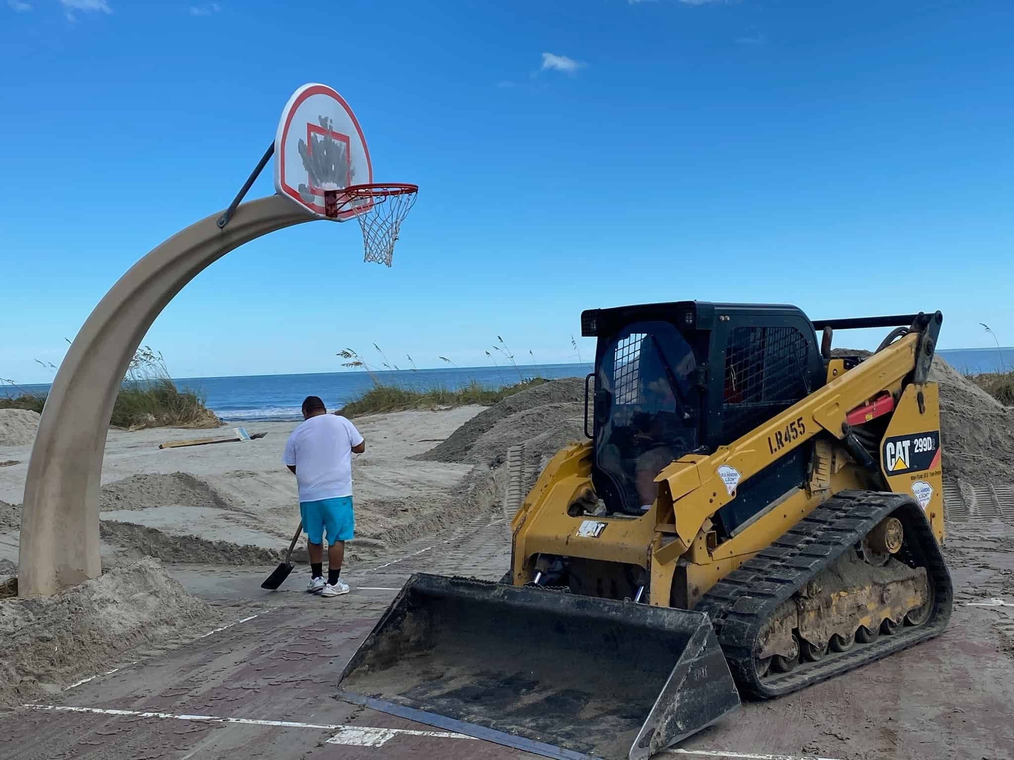 A bulldozer at Ocean Lakes campground cleaning up the sand next to a basketball court.