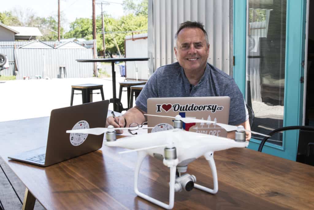 The CEO of an RV Industry company enjoys working outdoorsy, sitting at a table with a laptop and a DJI drone.