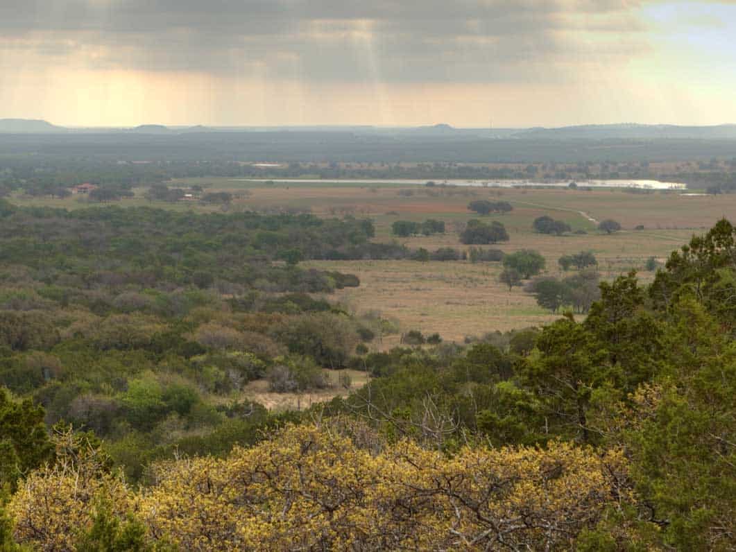 A picturesque view from a hill overlooking an open field and lush trees in North Texas.