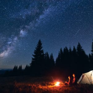 A person is camping under a starry sky at Louisiana State Parks with a tent in the background, enjoying overnight stays.