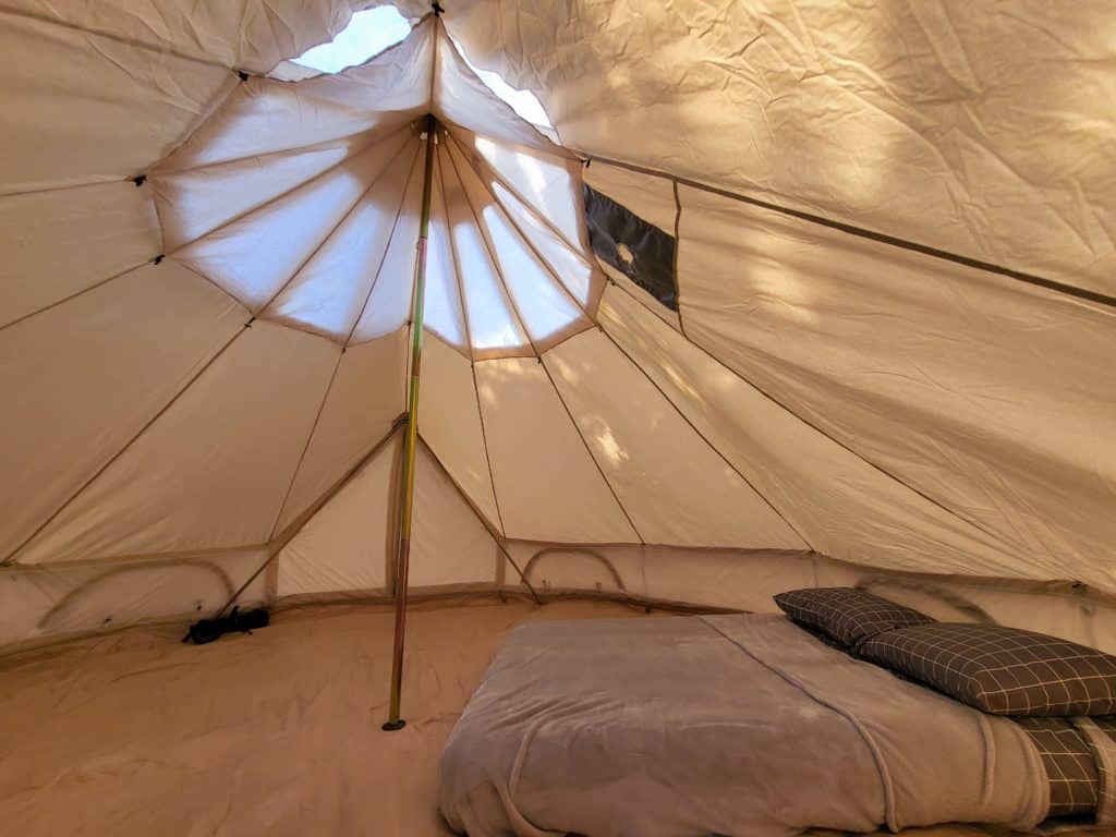 The inside of a white tent with a bed inside, part of the BLK Dream Camp.