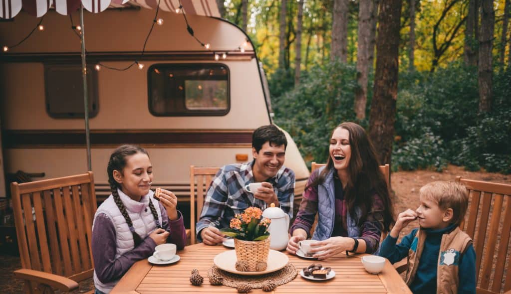 A family sits at a table in front of an RV, enjoying their vacation.