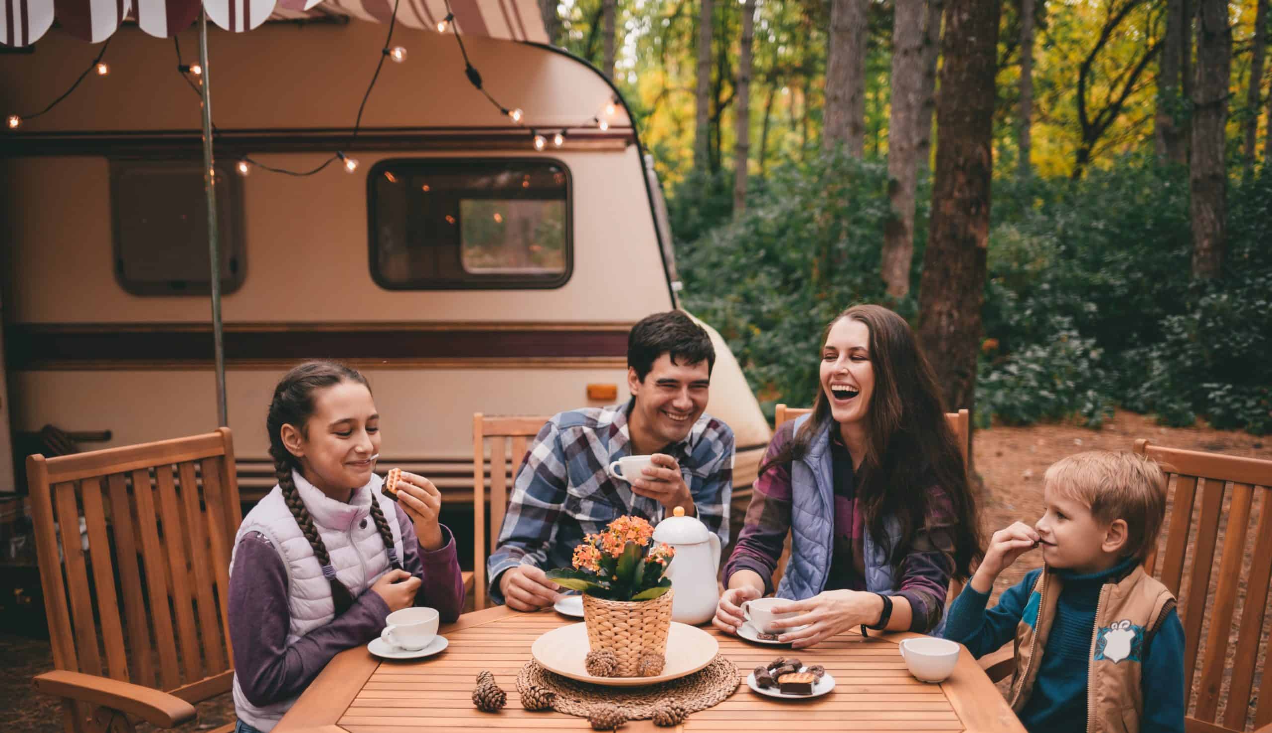 A family sits at a table in front of an RV, enjoying their vacation.