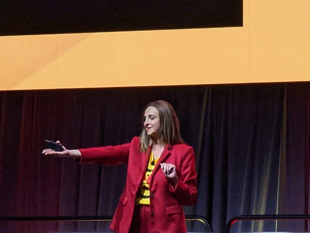 A woman in a red suit confidently stands on stage at the Special Networking Reception for Convention First-Timers organized by KOA.