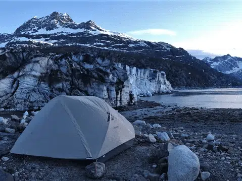 A tent pitched in front of a lake with mountains in the background, showcasing the breathtaking scenery of Glacier Bay National Park.