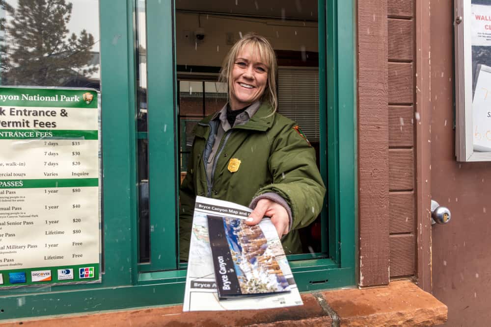 A woman holding a newspaper in front of a store, reading about the National Park Service's 2023 Free Admission Days.