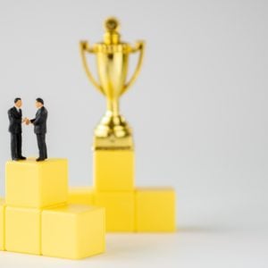 Two KEI founders, standing on top of yellow cubes, proudly display their Lifetime Achievement Award trophy.