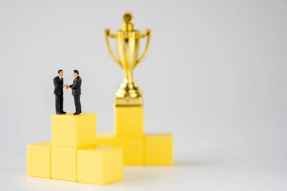 Two KEI Founder businessmen standing on top of yellow cubes with a Lifetime Achievement Award trophy.
