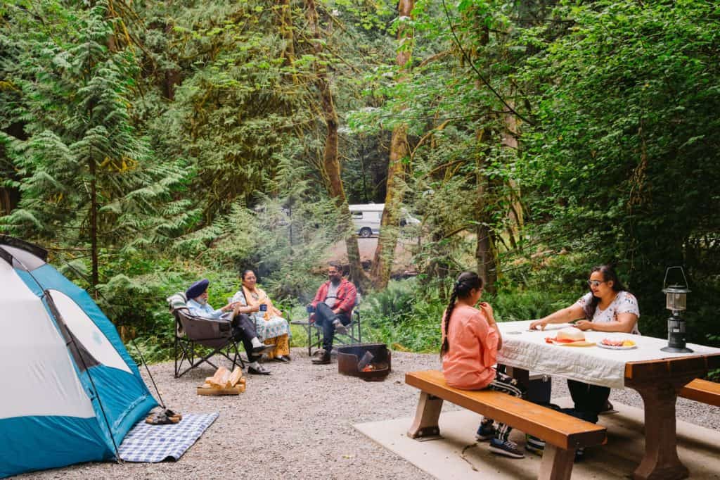 Description: A group of people sitting around a picnic table in a BC Parks wooded area.
Keywords: BC Parks