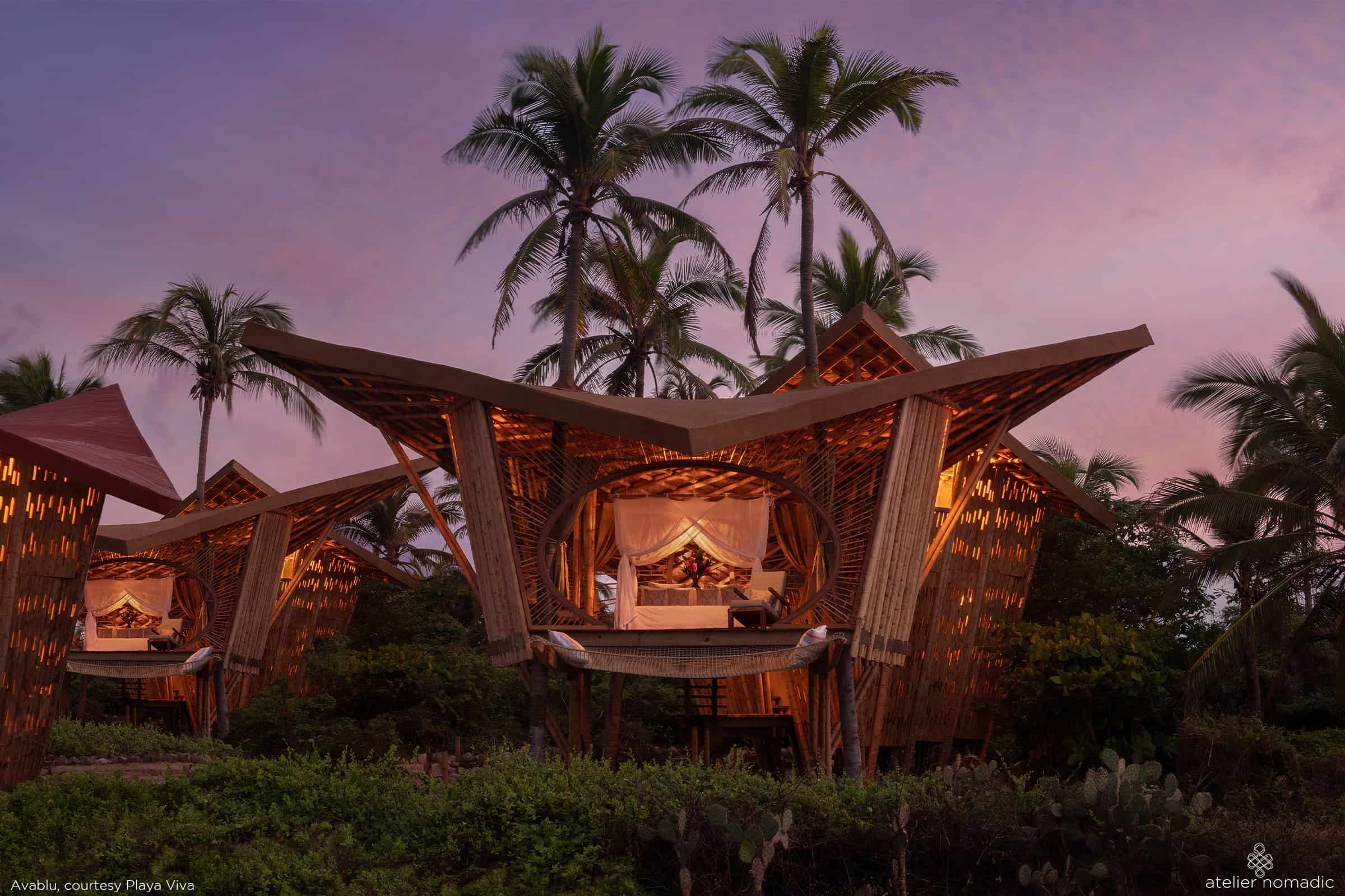 Two Nomadic Resorts tree houses in the middle of the jungle at dusk, offering a unique hospitality experience.