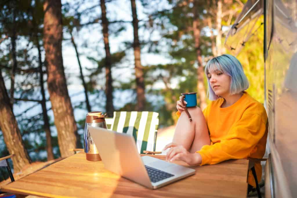 A Millennial woman sitting at a table with a laptop and a cup of coffee.