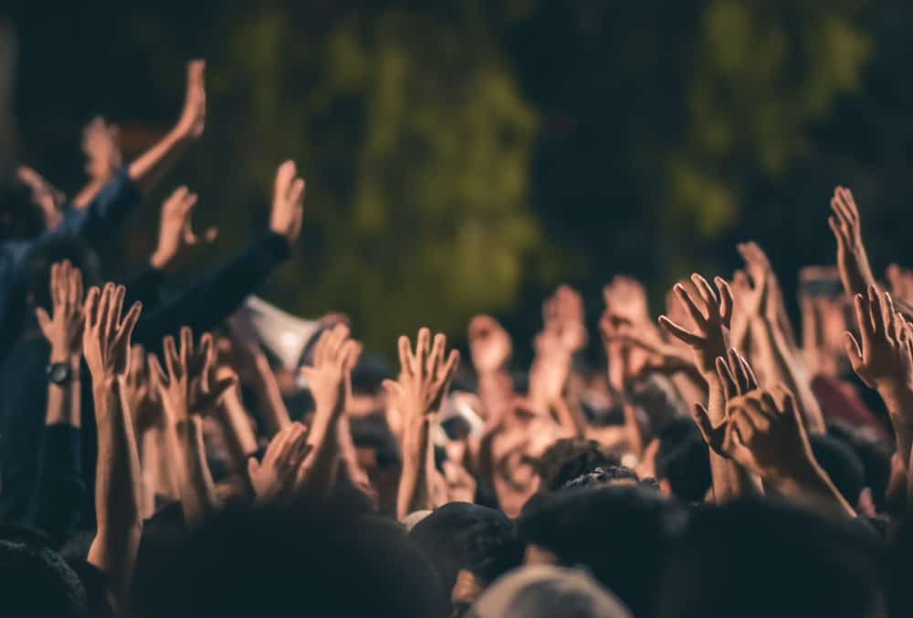 A crowd of people raising their hands in protest at a concert, expressing their disagreement with the Dartmoor wild camping ban.