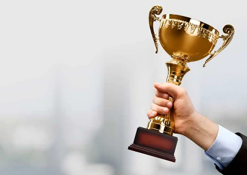 A hand holding a gold trophy at the 2023 CCRVC COHCE Award Nominations event in front of a cityscape.