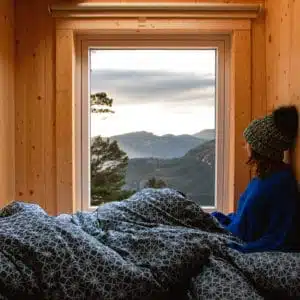 A woman is sitting in a bed with a view of mountains while glamping.