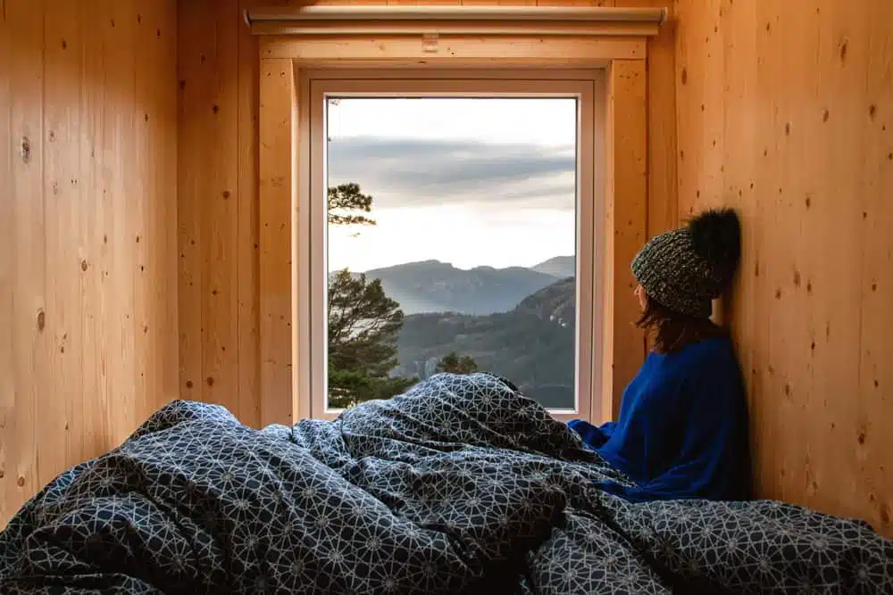 A woman is sitting in a bed with a view of mountains while glamping.