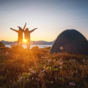 Two people leading a camping expedition in Europe, standing in front of a tent at sunset.
