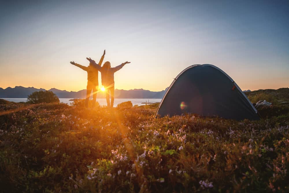 Two people leading a camping expedition in Europe, standing in front of a tent at sunset.