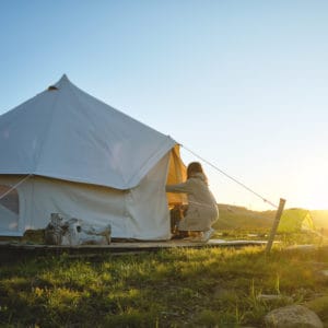 A woman sits in a glamping tent at sunset, enjoying the tranquil beauty of nature.
