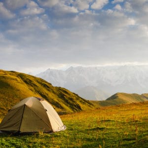 A tent pitched in a grassy field with mountains in the background. The perfect scene for a serene camping experience in Europe with LeadingCampings.