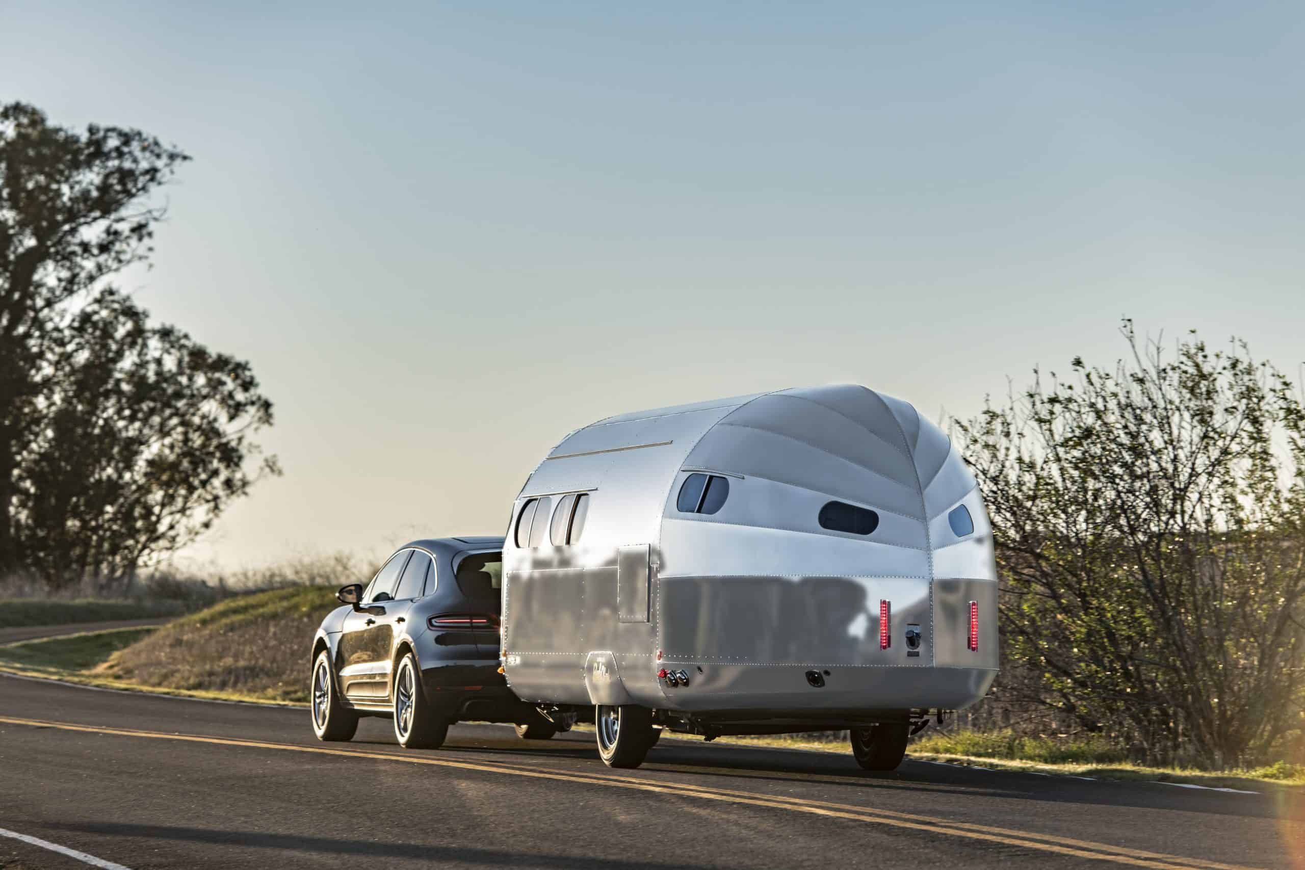 An affordable travel trailer is pulled behind a car on a country road.