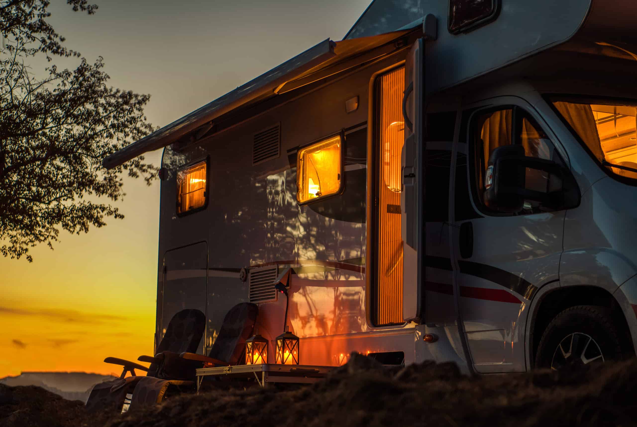 A white rv from Camping World Holdings Inc. is parked in a field at sunset.