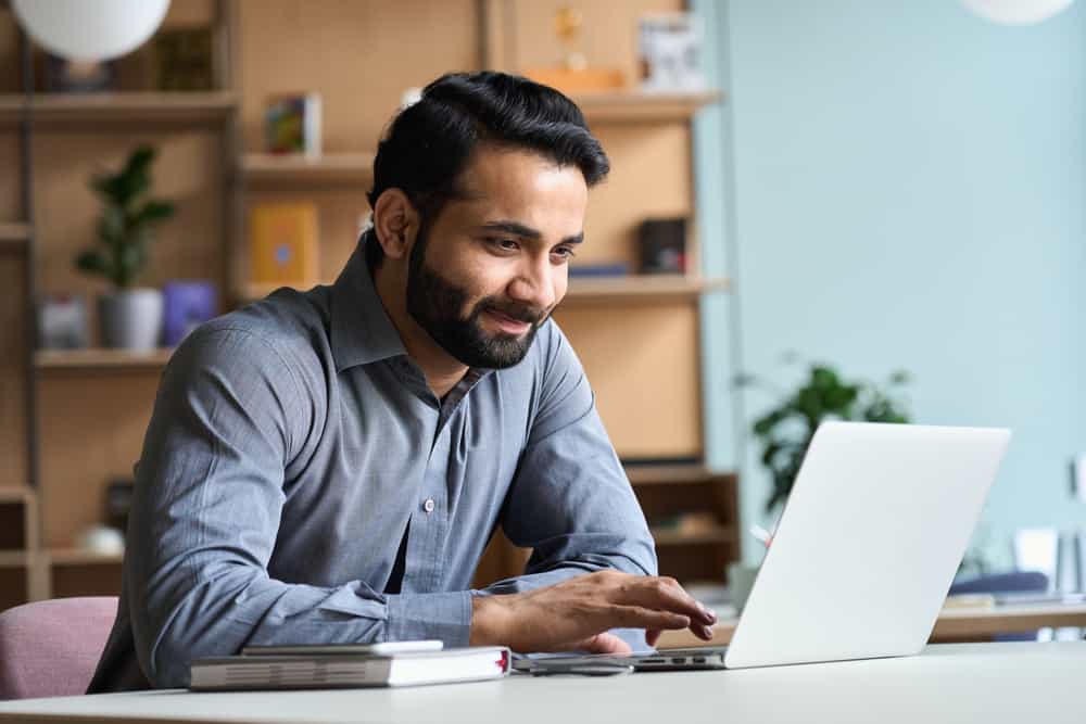 A man experiencing unmatched convenience while working on his laptop in an office, with the instant answers provided by an AI chatbot.