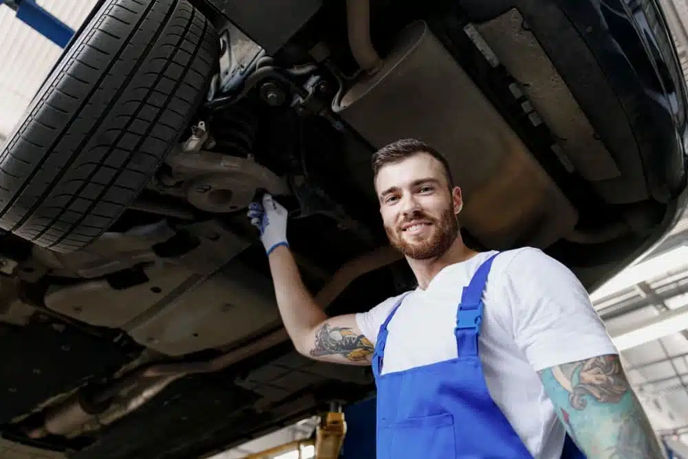 A mechanic standing under a car in a garage who received training at the RV Technical Institute.