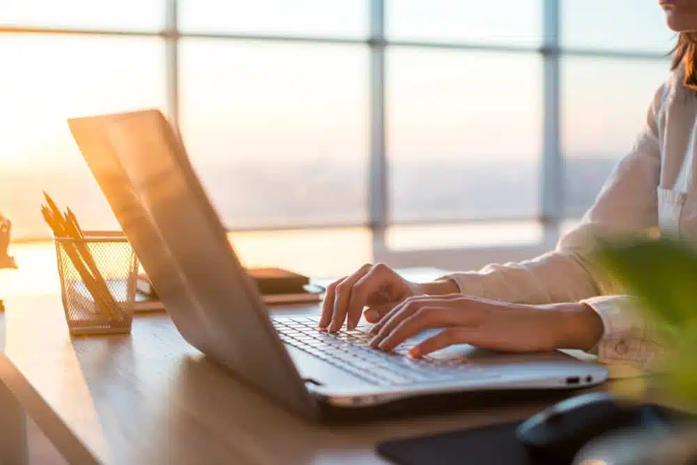 A woman experiencing unmatched convenience as she types on a laptop in front of a window at the Verde Ranch RV Resort.