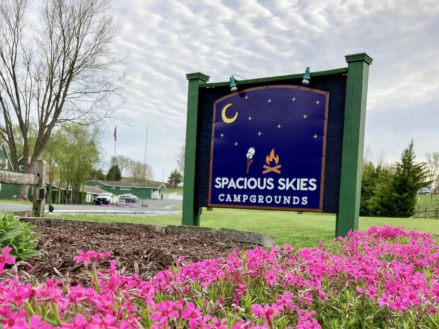 A sign for Spacious Skies Campgrounds in front of pink flowers.