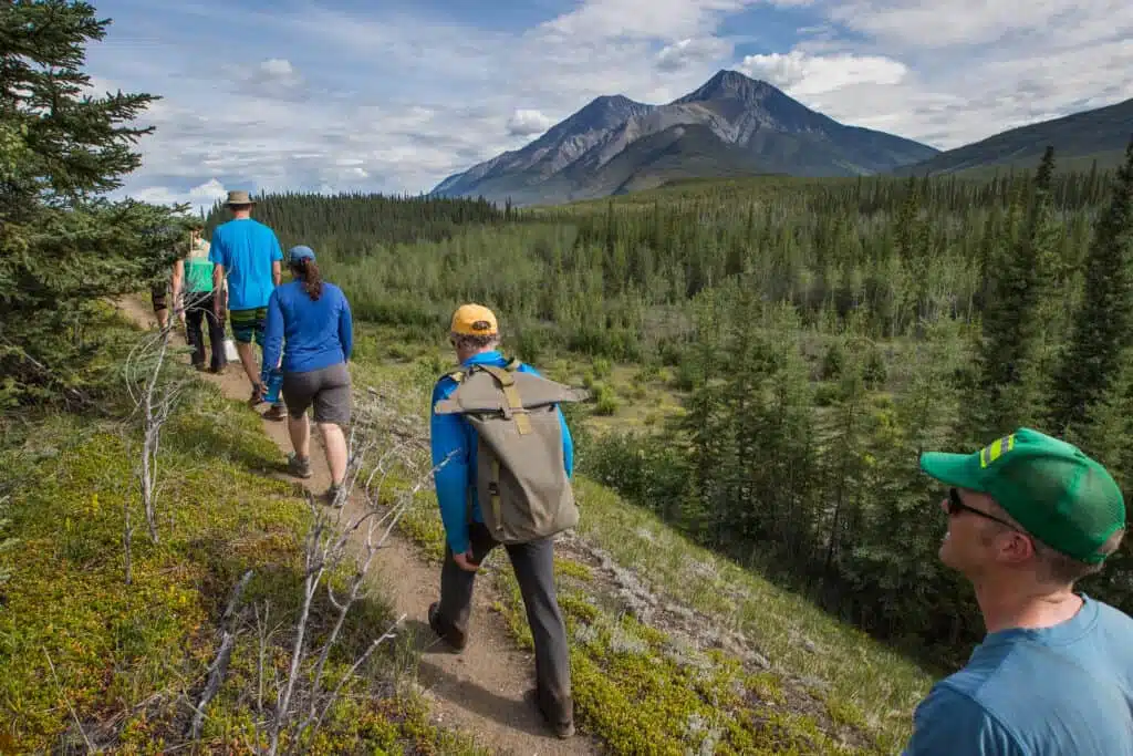 A group of people hiking on a trail with mountains in the background, enjoying the scenic beauty of NWT Parks.