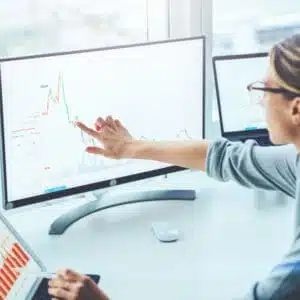 A Financial Analyst from IVEE Group is pointing at a graph on a computer screen in a team meeting.